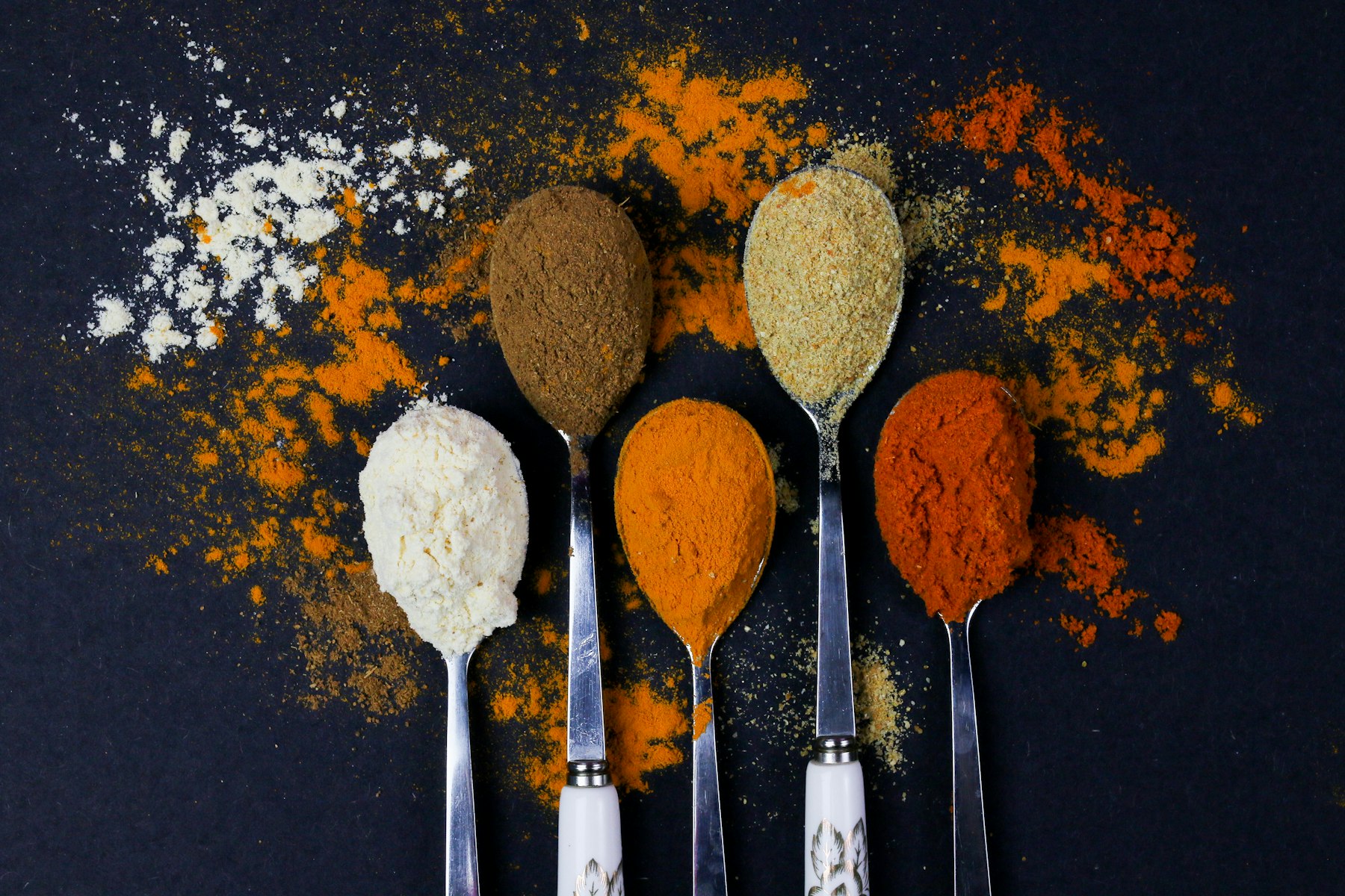 Ground and powdered spices in spoons on a dark surface