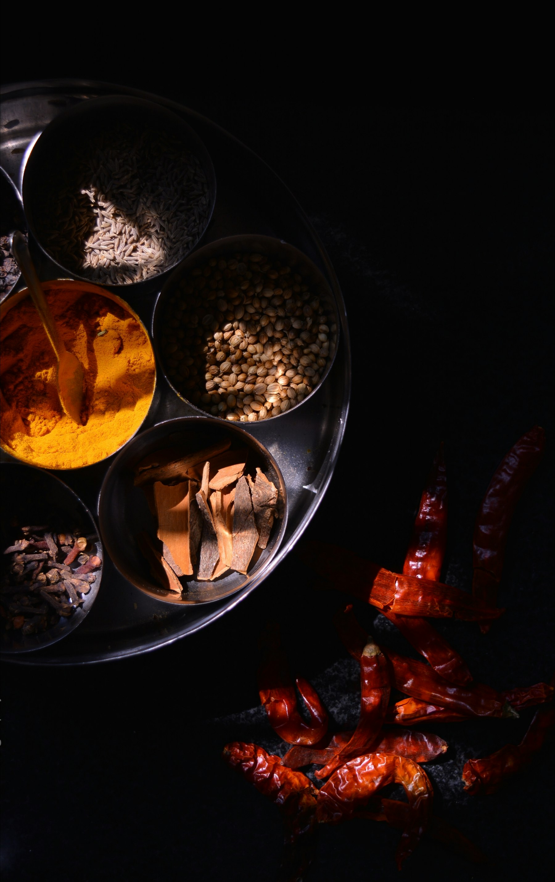 A traditional Indian spice box of turmeric, cumin and coriander beside dried red chillies